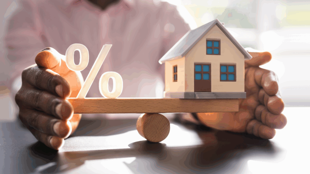 Hands holding a wood home and interest rate sign indicating a balance of interest rates vs purchase price